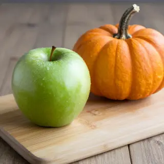 A green apple and an orange pumpkin on a wooden cutting boar