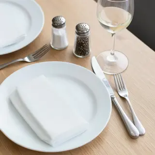 A dinner table scene with a plate, fork, knife, wine glass, 