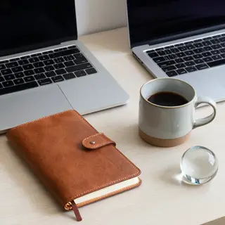 A workspace desk with a brushed aluminum laptop, a leather-b