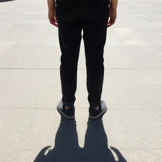 A person standing outdoors at midday with a short shadow dir