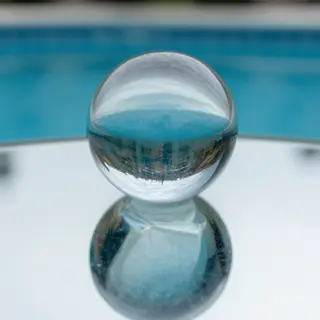 A clear glass sphere sitting on a mirror surface near a pool