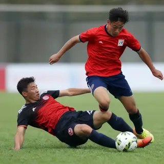 Two soccer players mid-tackle, one sliding and the other jum