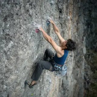 A rock climber clinging to a cliff face with arms and legs e