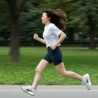 A woman mid-stride running through a park, hair and clothes 
