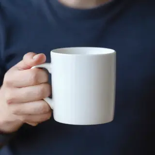A person holding a white ceramic coffee mug by the handle wi