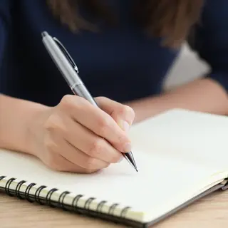 A woman writing in a notebook with a pen gripped correctly i