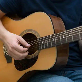 A person playing an acoustic guitar with left hand on the fr