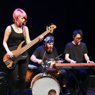 Three musicians on stage: a tall woman with short pink hair 