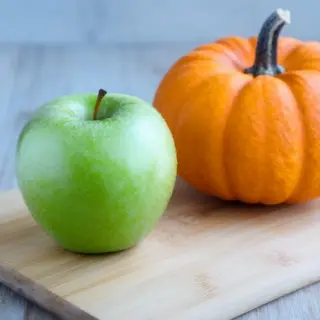 A green apple and an orange pumpkin on a wooden cutting boar