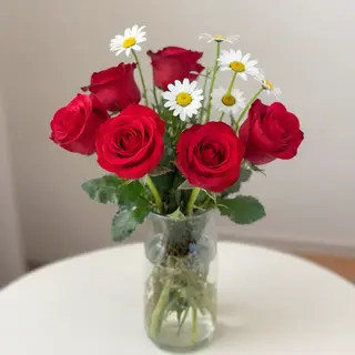 4 red roses and 2 white daisies in a glass vase on a table