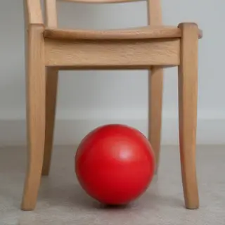 A red ball underneath a wooden chair