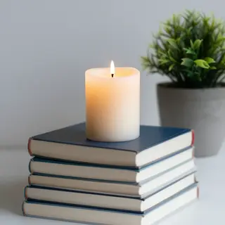 A candle on top of a stack of books, the books next to a pot