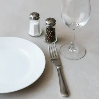 A dinner table scene with a plate, fork, knife, wine glass, 