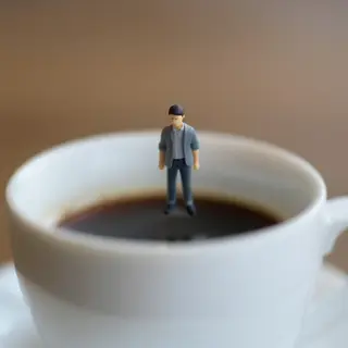 A tiny person standing on the rim of a coffee cup, looking d
