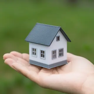 A miniature house sitting on the palm of someone's hand