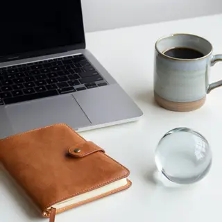 A workspace desk with a brushed aluminum laptop, a leather-b