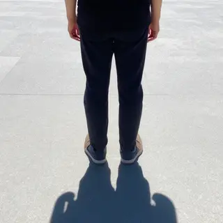 A person standing outdoors at midday with a short shadow dir