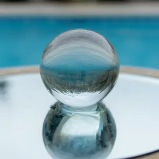 A clear glass sphere sitting on a mirror surface near a pool