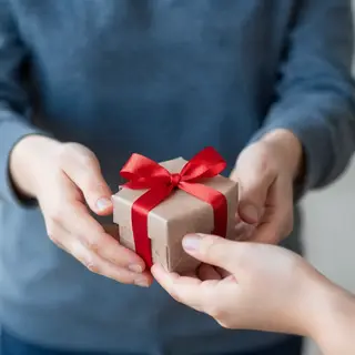One person handing a small gift box to another person, both 