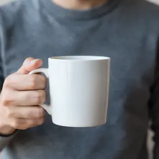 A person holding a white ceramic coffee mug by the handle wi