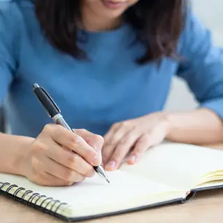 A woman writing in a notebook with a pen gripped correctly i