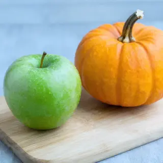 A green apple and an orange pumpkin on a wooden cutting boar