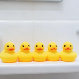 Exactly 5 yellow rubber ducks sitting in a row on a bathroom