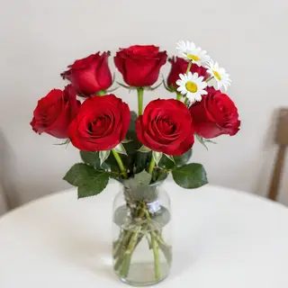 4 red roses and 2 white daisies in a glass vase on a table