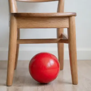 A red ball underneath a wooden chair