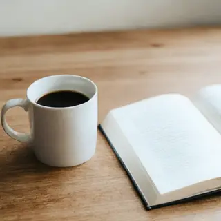 A coffee mug next to an open book on a desk