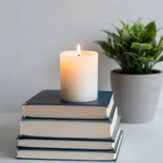 A candle on top of a stack of books, the books next to a pot