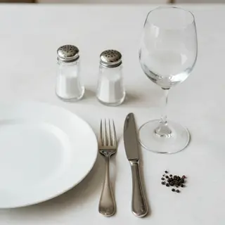 A dinner table scene with a plate, fork, knife, wine glass, 