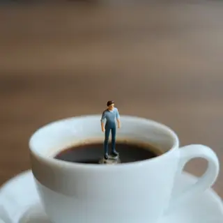 A tiny person standing on the rim of a coffee cup, looking d