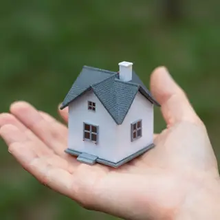 A miniature house sitting on the palm of someone's hand