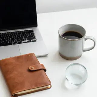 A workspace desk with a brushed aluminum laptop, a leather-b