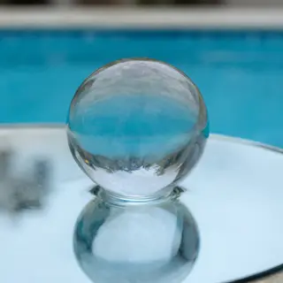 A clear glass sphere sitting on a mirror surface near a pool