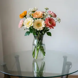 A vase of flowers on a glass table with a clear reflection v