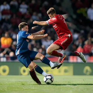 Two soccer players mid-tackle, one sliding and the other jum