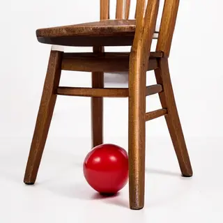 A red ball underneath a wooden chair