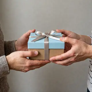 One person handing a small gift box to another person, both 