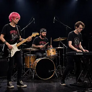 Three musicians on stage: a tall woman with short pink hair 