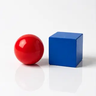 A red ball and a blue cube sitting side by side on a white s