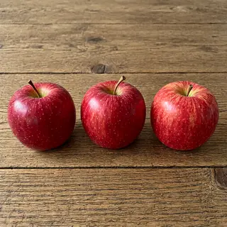 Exactly 3 red apples arranged on a wooden table