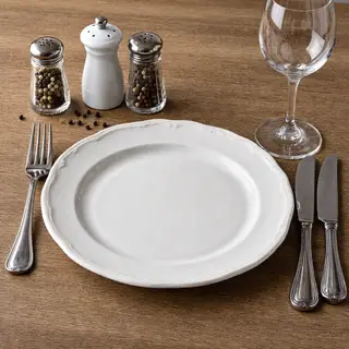A dinner table scene with a plate, fork, knife, wine glass, 