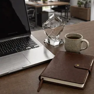 A workspace desk with a brushed aluminum laptop, a leather-b
