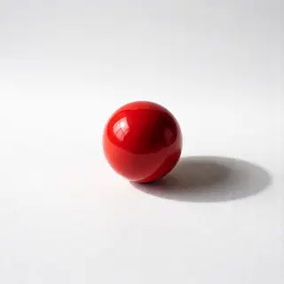 A red sphere on a white surface with a single shadow cast to