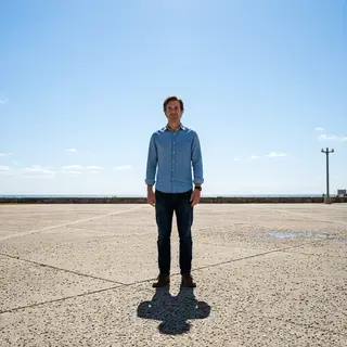 A person standing outdoors at midday with a short shadow dir