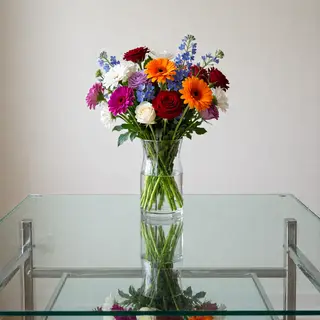 A vase of flowers on a glass table with a clear reflection v
