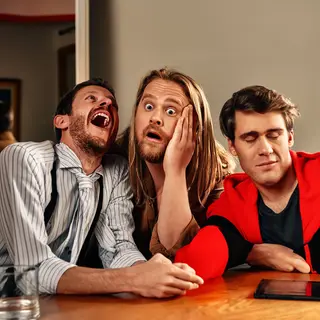 A group of three friends at a table: one laughing with head 