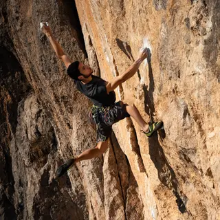 A rock climber clinging to a cliff face with arms and legs e
